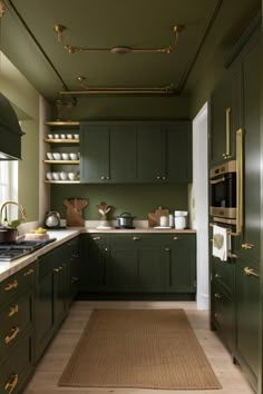 a kitchen with green cabinets and gold trimmings on the walls, along with an area rug