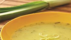 a yellow bowl filled with soup next to some celery stalks on a table