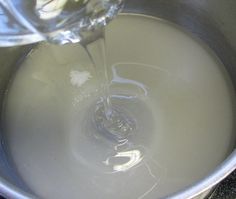 water is being poured into a metal pot with white liquid in it and an orange slice on the side