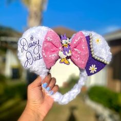 a hand holding up a minnie mouse ears headband with the word disney on it