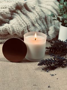 a white candle sitting on top of a table next to a pot filled with plants