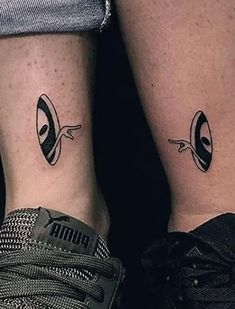 two people with matching tattoos on their legs, one has an alien head and the other is