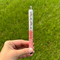 a person holding up a pink and white stick with writing on it in the grass