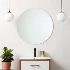 a bathroom vanity with a round mirror on the wall above it and a potted plant next to it