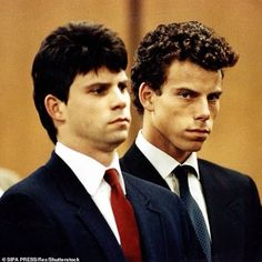 two men in suits and ties standing next to each other with one looking at the camera