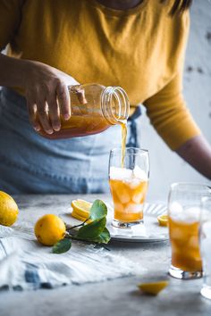 a woman pouring orange juice into a glass on top of a table next to lemons