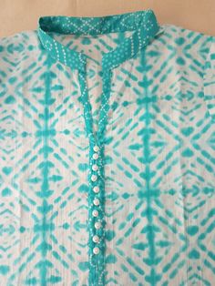 a blue and white shirt that has some beads on the front, and a green tie around the neck