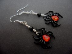 black spider earrings with red glass eyes and silver earwires on a dark surface