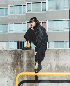 a woman sitting on top of a cement wall next to a yellow rail and building