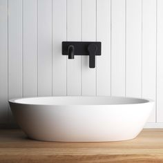 a large white bowl sink sitting on top of a wooden floor next to a wall mounted faucet