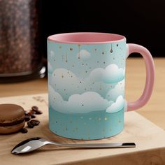 a pink and blue coffee mug sitting on top of a wooden table next to a cookie