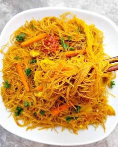 a white plate topped with noodles and carrots next to chopsticks on a table