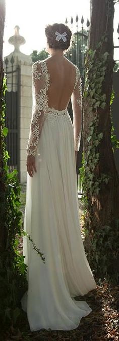 the back of a woman's wedding dress in front of some trees and bushes