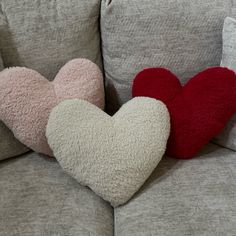 two heart shaped pillows sitting on the back of a couch with grey and red cushions