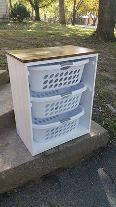 a white cabinet with three baskets on top of it in front of some trees and grass