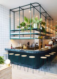 the interior of a restaurant with green plants and bar stools in front of it