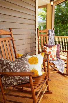 two wooden rocking chairs sitting on top of a wooden floor next to a porch covered in pillows