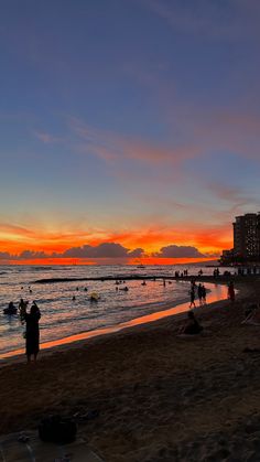 people are on the beach at sunset with buildings in the backgrouds and water