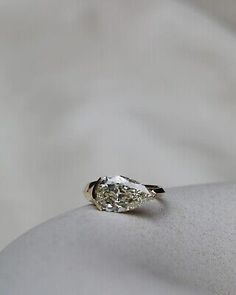 an engagement ring with a pear shaped diamond in the center on a white cloth background