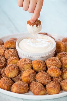 a person dipping something into some kind of sauce on top of doughnuts that are sitting on a plate