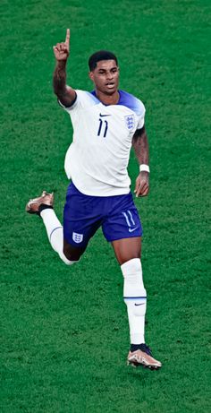 a man kicking a soccer ball on top of a green field with his hand in the air