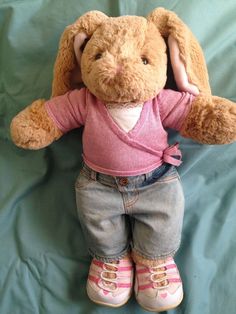 a teddy bear with pink shirt and jeans on it's legs, sitting in front of a blue sheet