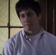 a man standing in front of a window wearing a white shirt and looking at the camera