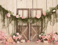 an arrangement of pink flowers and greenery on a wooden table in front of a barn door