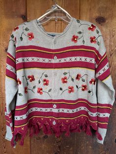 a sweater with flowers and fringes hanging on a wooden wall