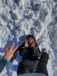 two people sitting in the snow with their hands up and one person standing next to them