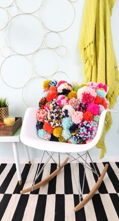 a white rocking chair filled with lots of colorful pom - poms on top of a black and white striped rug