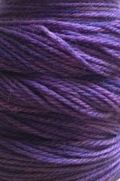 purple yarn is spooled on top of a white surface with the thread in it