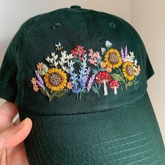 a green hat with flowers embroidered on the front and side, held up by a person's hand