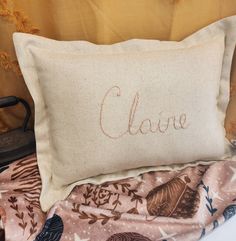 a close up of a pillow with the word clarie on it next to an ironing board