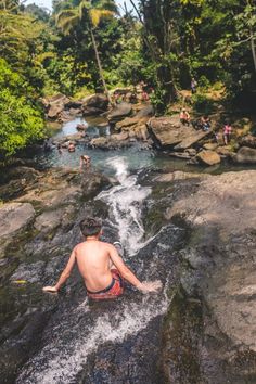 a man sitting on top of a rock next to a small waterfall in the forest