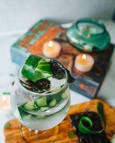 a glass filled with water and green plants on top of a wooden cutting board next to candles