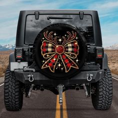 a black jeep with red and gold bows on it's front tire cover in the middle of a road