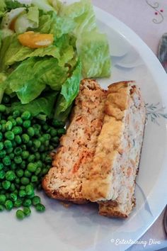 a white plate topped with meat, peas and lettuce next to a salad