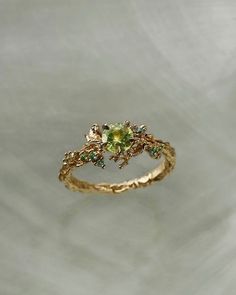 a yellow gold ring with green stones and leaves on the band, set against a white background