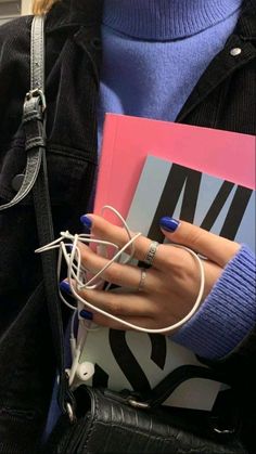 a woman with blue nails holding a book and headphones in her hand while wearing a black jacket