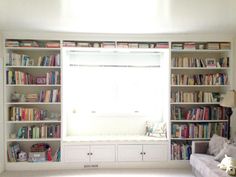 a living room filled with lots of books on top of white bookcases next to a window