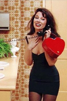 a woman holding a red heart and talking on the phone while standing in a kitchen