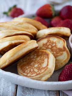 some pancakes and strawberries in a white bowl on a wooden table next to dipping sauce