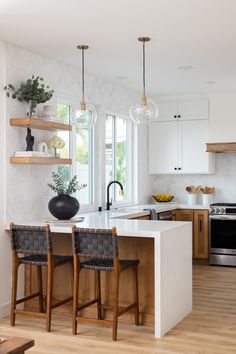 a kitchen with white counter tops and wooden chairs in front of an island that has two black vases on it