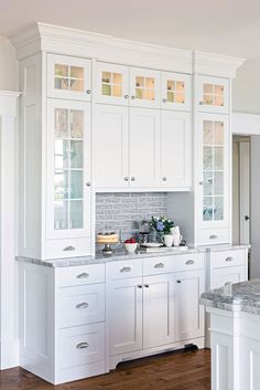 a kitchen with white cabinets and marble counter tops