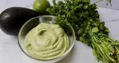 an avocado, cilantro and limes on a marble counter top