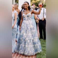 a woman in a blue and white dress standing next to other people on a brick walkway