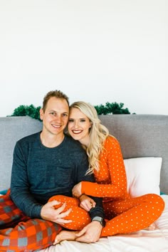 a man and woman sitting on top of a bed smiling at the camera with their arms around each other