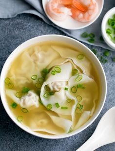 two bowls filled with dumplings and veggies on top of a gray table