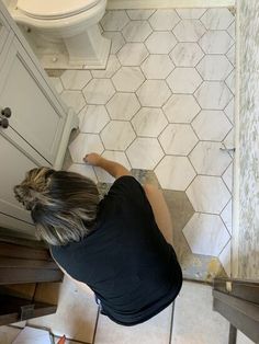 a woman kneeling down on the floor in front of a bathroom sink while painting tile